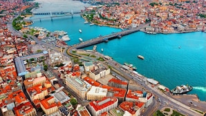 An aerial view of a coastal city with a prominent bridge, dense urban area, and a marina with boats. - Galata Sea Suites (İstanbul)