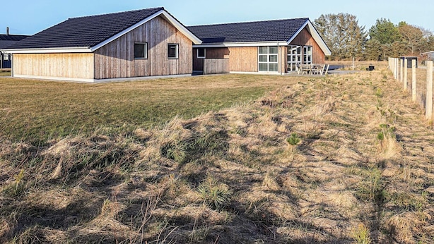 Ein zweistöckiges Holzhaus mit geneigtem Dach, einer Veranda und einem umzäunten Garten.