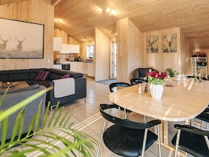 A modern interior with a wooden ceiling, a dining area with a round table and chairs, a sofa, and a kitchen in the background. - 5 Star Holiday Home in Brovst (Brovst)
