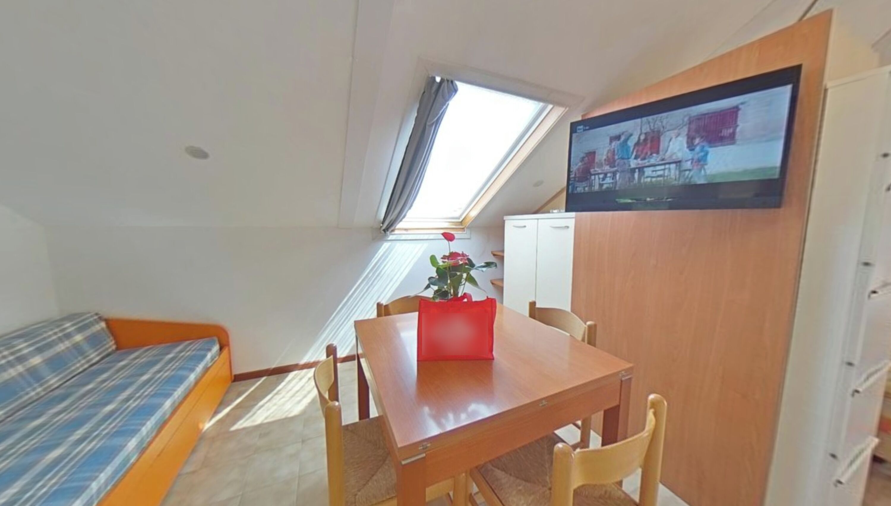 A compact room with a bed, a dining table, a TV, and a window.