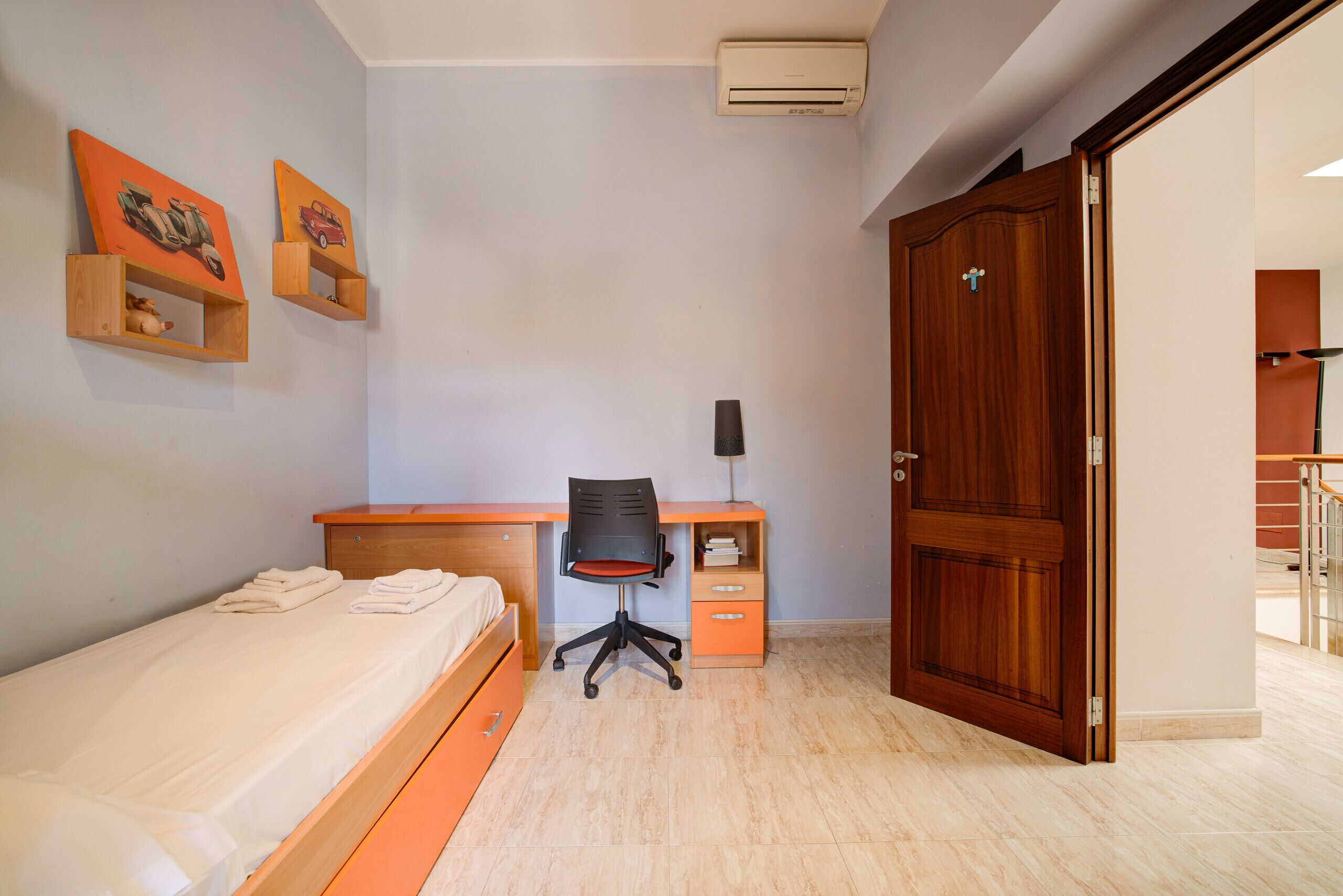 Un dormitorio con cama, escritorio, silla, armario y puerta.