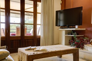 Een kamer met een houten tafel, een open boek, een televisie en uitzicht door een glazen deur.