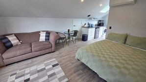 Un espace de vie compact comprenant un canapé, un lit, un coin repas et une kitchenette.