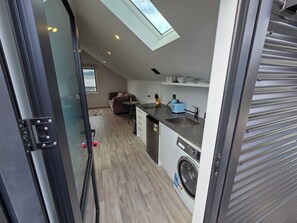 A compact kitchen with a washing machine, a toaster, and a small dining area with a sofa. - Warm Near new Studio Flat (Jacks Point)
