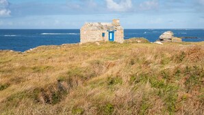 A stone cottage with a blue door, situated on a grassy cliff overlooking the sea. - Plouguerneau Coastal Retreat With Garden (Lampaul-Plouarzel)