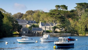 A calm harbor with boats, stone buildings, and lush greenery. - Plouguerneau Coastal Retreat With Garden (Lampaul-Plouarzel)