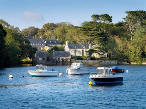 A calm harbor with boats, stone buildings, and lush greenery. - Plouguerneau Coastal Retreat With Garden (Lampaul-Plouarzel)