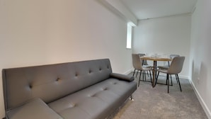 A modern living room with a grey sofa, a dining table with chairs, and a window. - WorkStay Portsmouth Contractor House (Portsmouth)