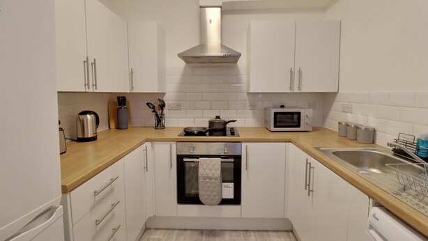 A modern kitchen with white cabinets, a stainless steel range hood, a microwave, a sink, and a dishwasher. - WorkStay Portsmouth Contractor House (Portsmouth)