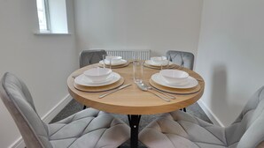 A dining table set for four with white plates, silverware, and a glass. - WorkStay Portsmouth Contractor House (Portsmouth)