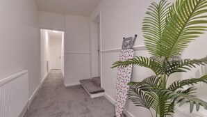 A hallway with a radiator, a grey carpet, a grey bench, a potted plant, and a door leading to another room. - WorkStay Portsmouth Contractor House (Portsmouth)