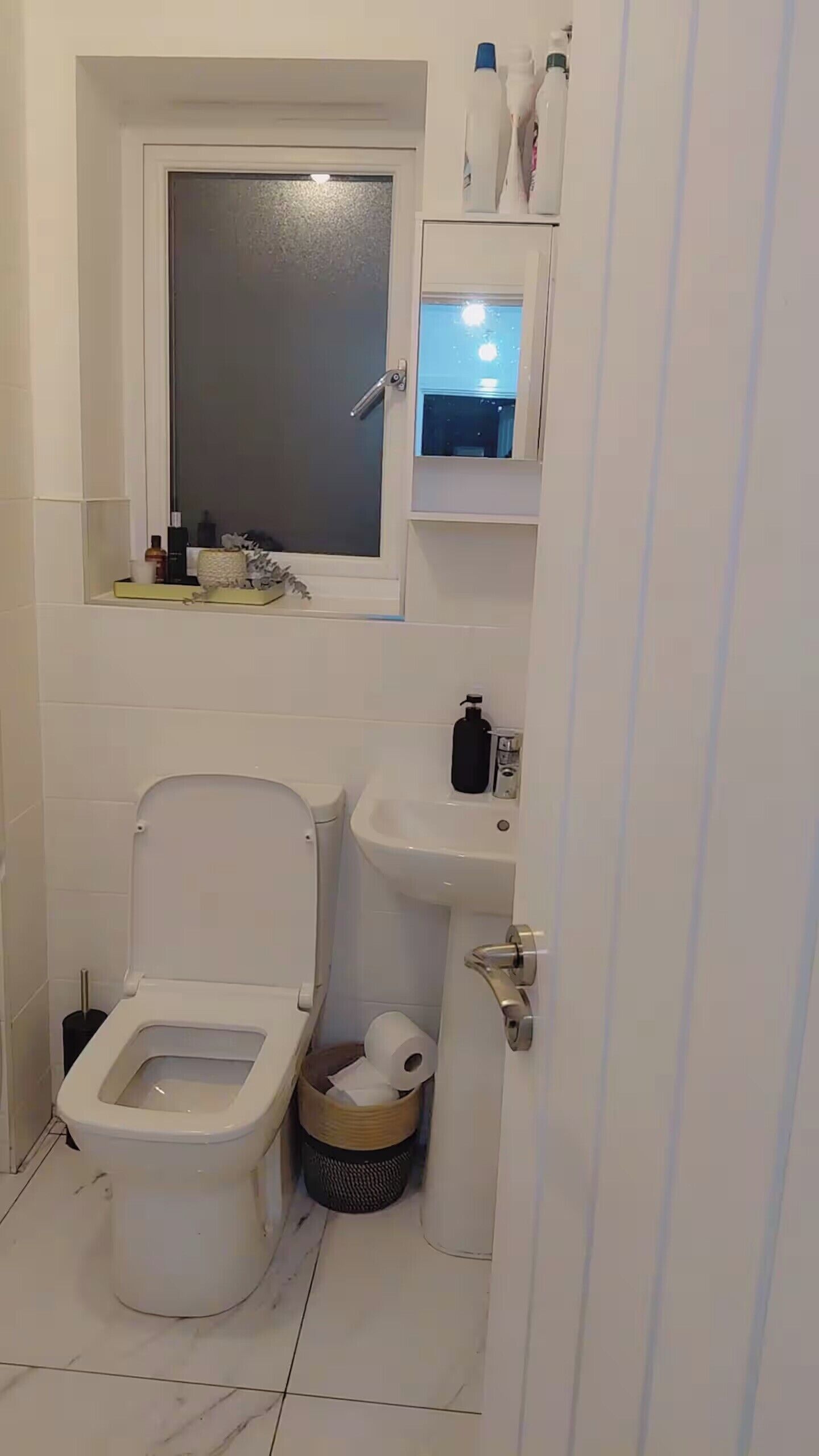 A bathroom with a toilet, bidet, sink, and a window above the sink.