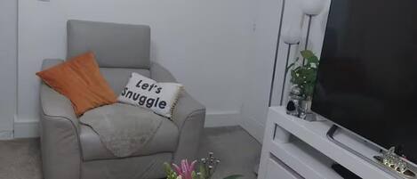 Una sala de estar con un sofá gris, un cojín naranja, un mueble para TV y una cita decorativa en la pared.