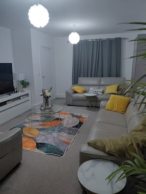 Un salon avec un canapé, une table basse, un téléviseur et une plante.