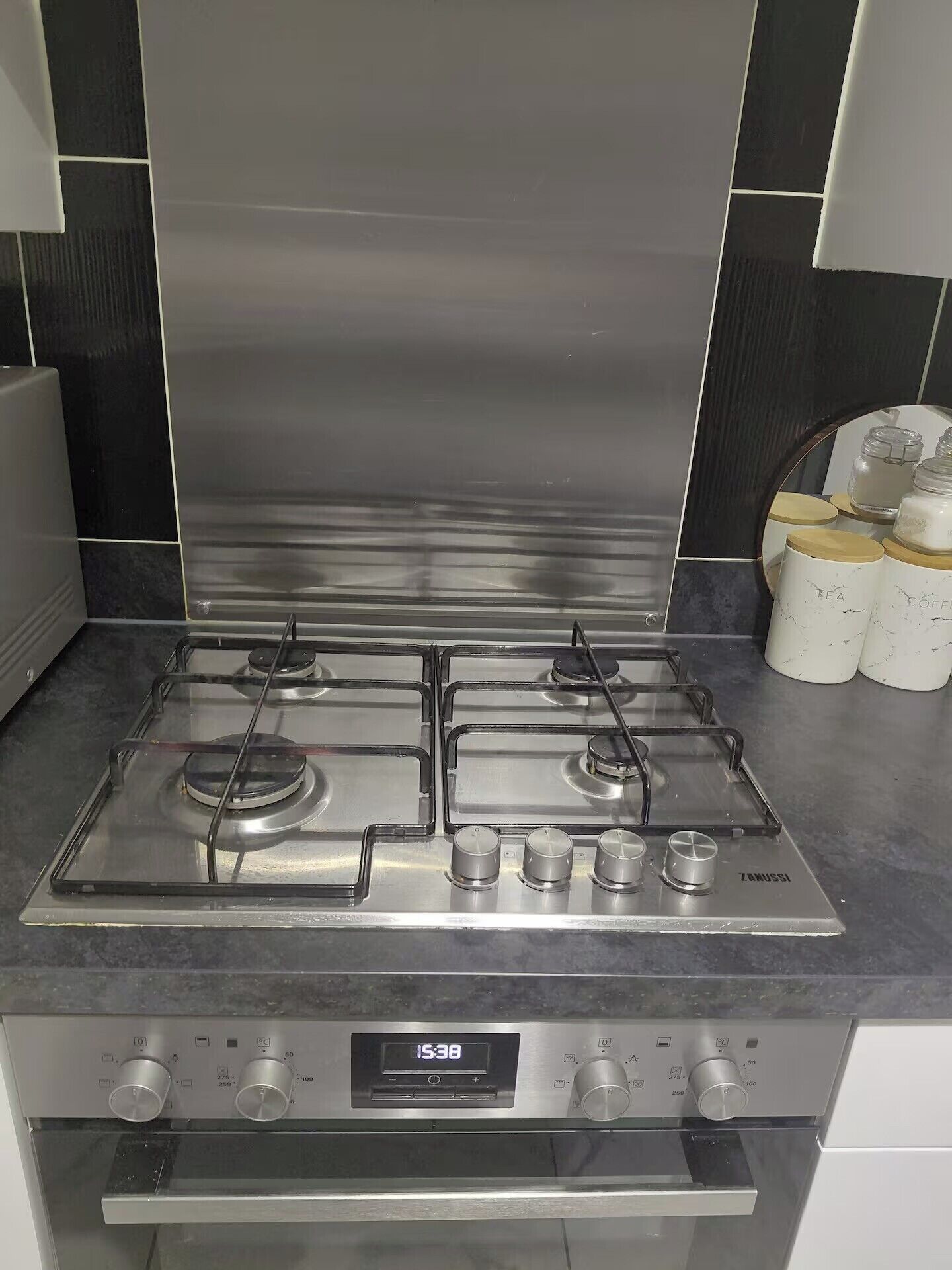 A modern kitchen with a stainless steel stove, a digital clock, and a set of white storage containers.