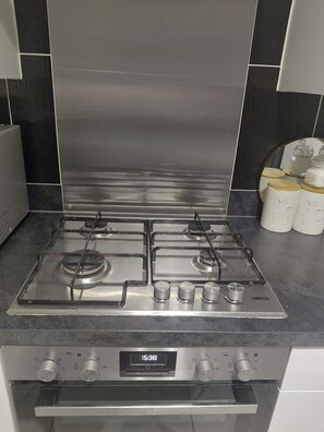 A modern kitchen with a stainless steel stove, a digital clock, and a set of white storage containers.
