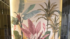 A red sofa, a white round table with a decorative item, and a wall with a tropical plant mural. - The Tulip Regency (Jaipur)