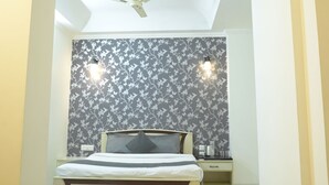 A bedroom with a bed, a ceiling fan, a nightstand, and a wall-mounted light fixture. - The Tulip Regency (Jaipur)