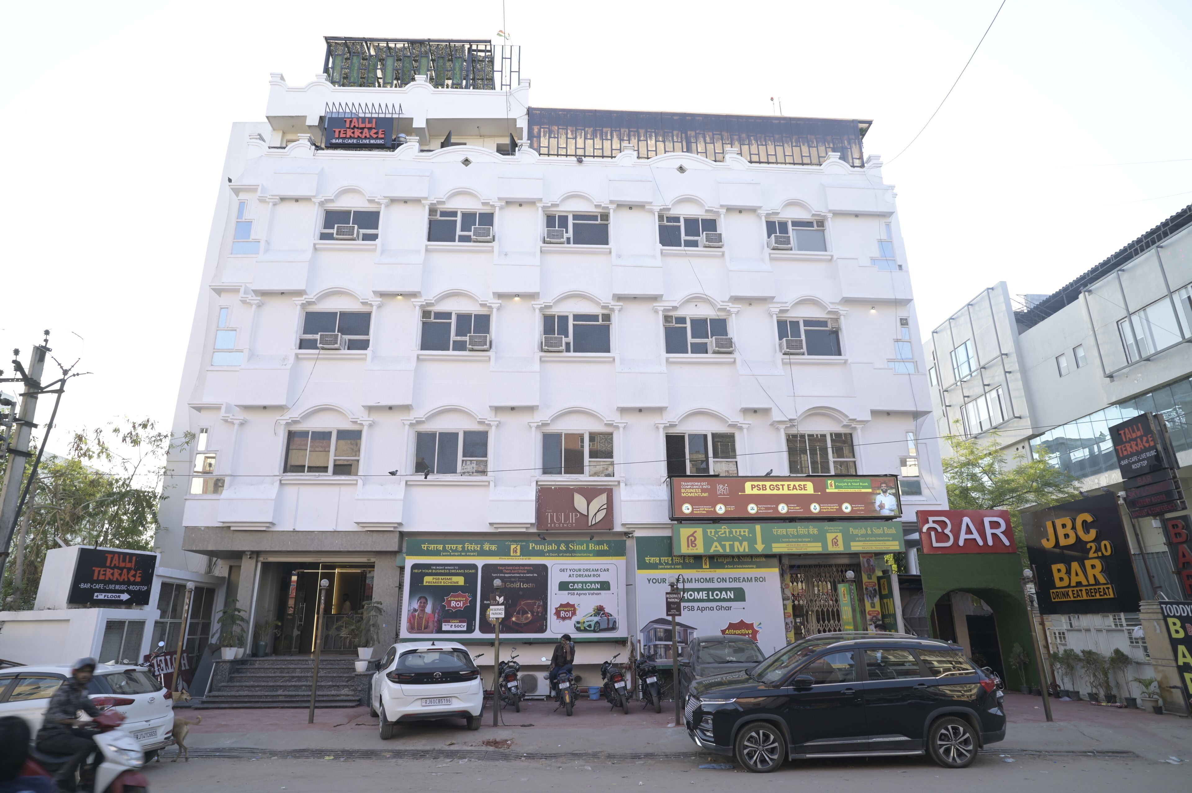 A multi-story building with a sign for Punjab & Sind Bank, a bar, and a JBC 2.0 Bar.
