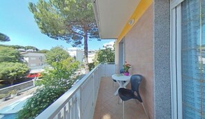 A balcony with a table and chairs, a potted plant, and a view of the surrounding buildings and trees. - Central Retreat Just a Short Walk From the Coast (Lignano Sabbiadoro)