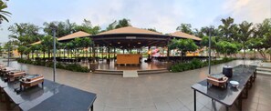 An outdoor dining area with covered tables and a central stage. - The Royal Retreat opp. Atal Sarovar (Rajkot)