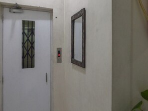 A white door with a geometric glass panel, a wall-mounted mirror, and a digital lock. - Innra Guest House (Kolkata)