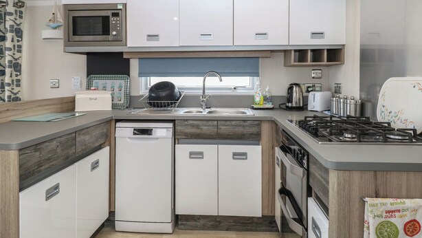 A compact kitchen with a microwave, sink, dishwasher, and stove. - Caravan 117 (Great Yarmouth)