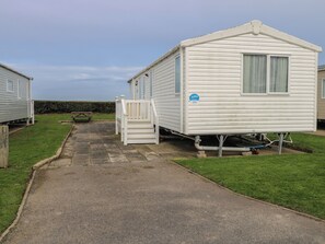 A caravan with a white exterior, a front porch, and a visible water pipe. - Caravan 117 (Great Yarmouth)