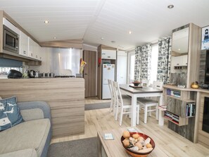 A modern kitchen with built-in appliances, a dining area with white chairs, and a cozy seating area with a sofa. - Caravan 117 (Great Yarmouth)