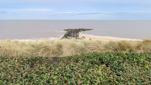 A coastal landscape with a rocky outcrop, sandy beach, and dense vegetation. - Caravan 117 (Great Yarmouth)