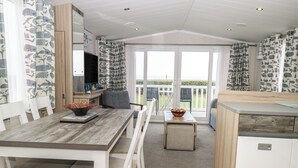 A modern kitchen with a dining area, white cabinetry, and a view of the sea. - Caravan 117 (Great Yarmouth)