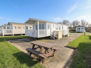 A caravan with a deck, a picnic table, and a small garden area. - Caravan 117 (Great Yarmouth)