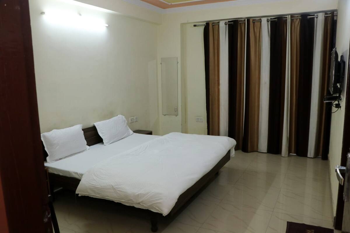 Habitación de hotel con cama, espejo, televisión y puerta que da a un balcón con cortinas.