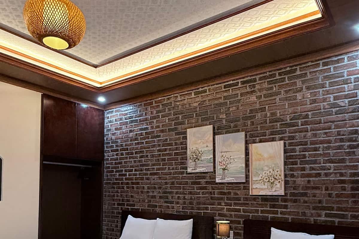 A hotel room with two beds, a brick wall, and a hanging light fixture.