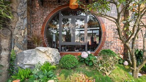A building with a circular window, stone wall, and a garden with various plants. - Tam Coc Green Vibes Retreat (Nam Hoa Lu)