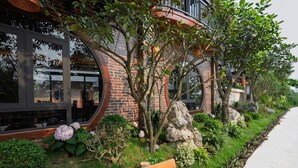 A brick building with large windows, a bench, and a well-maintained garden with various plants and rocks. - Tam Coc Green Vibes Retreat (Nam Hoa Lu)