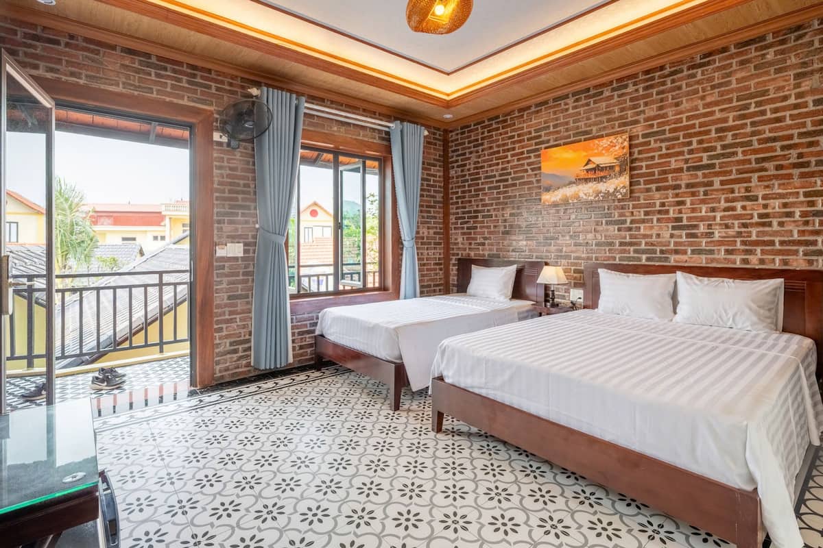 A hotel room with two beds, a balcony, and a brick wall.