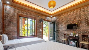 A room with a brick wall, a bed, a desk, and a TV. - Tam Coc Green Vibes Retreat (Nam Hoa Lu)