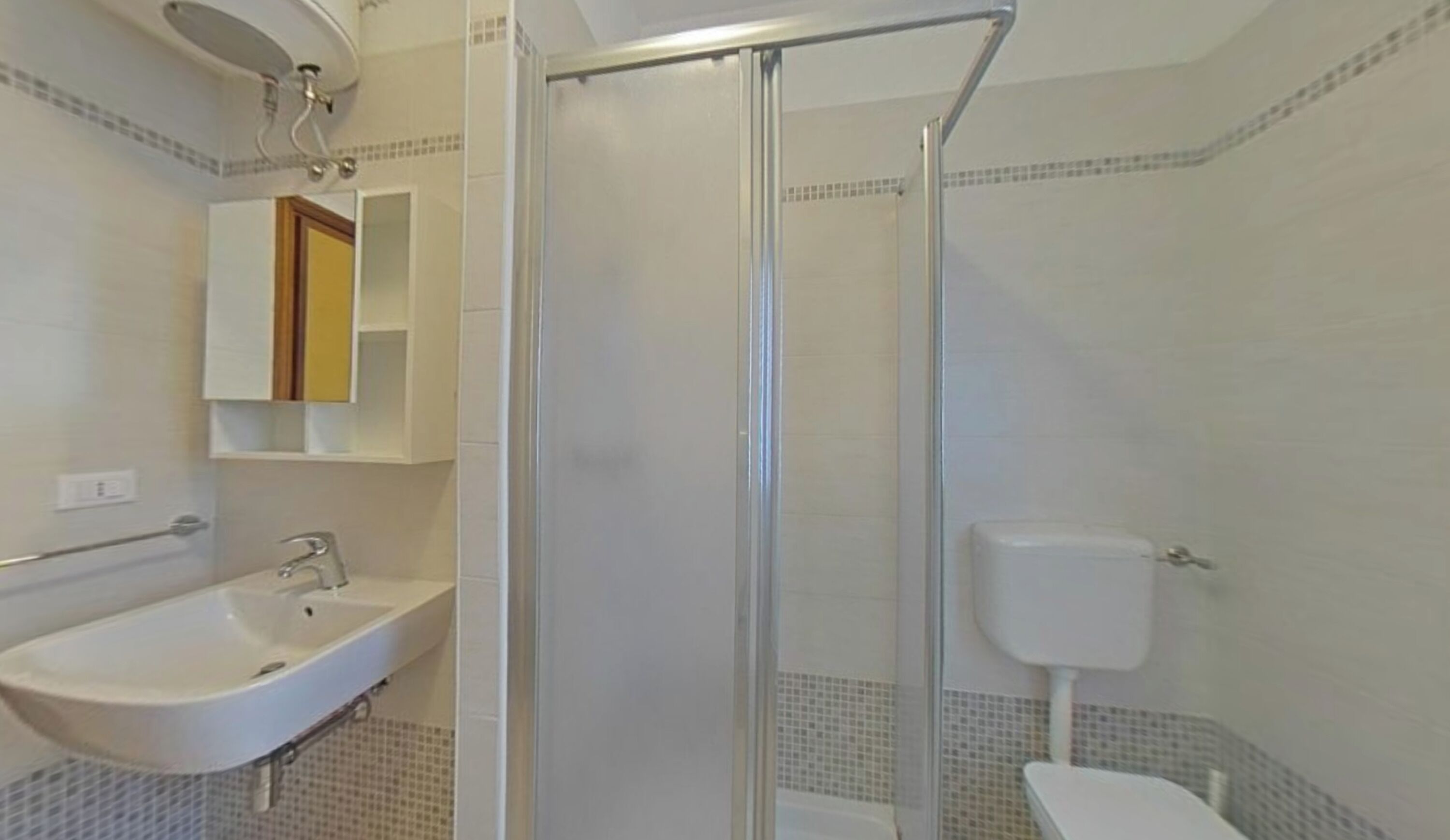 A bathroom with a shower, sink, toilet, and a mirror with a cabinet above.