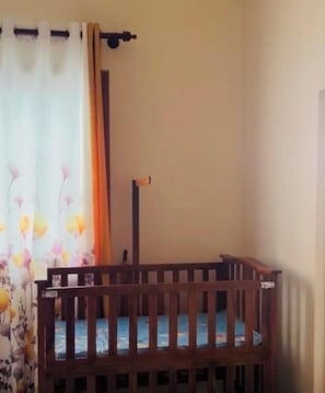 A room with a wooden crib, a curtain with floral patterns, and a plain wall.