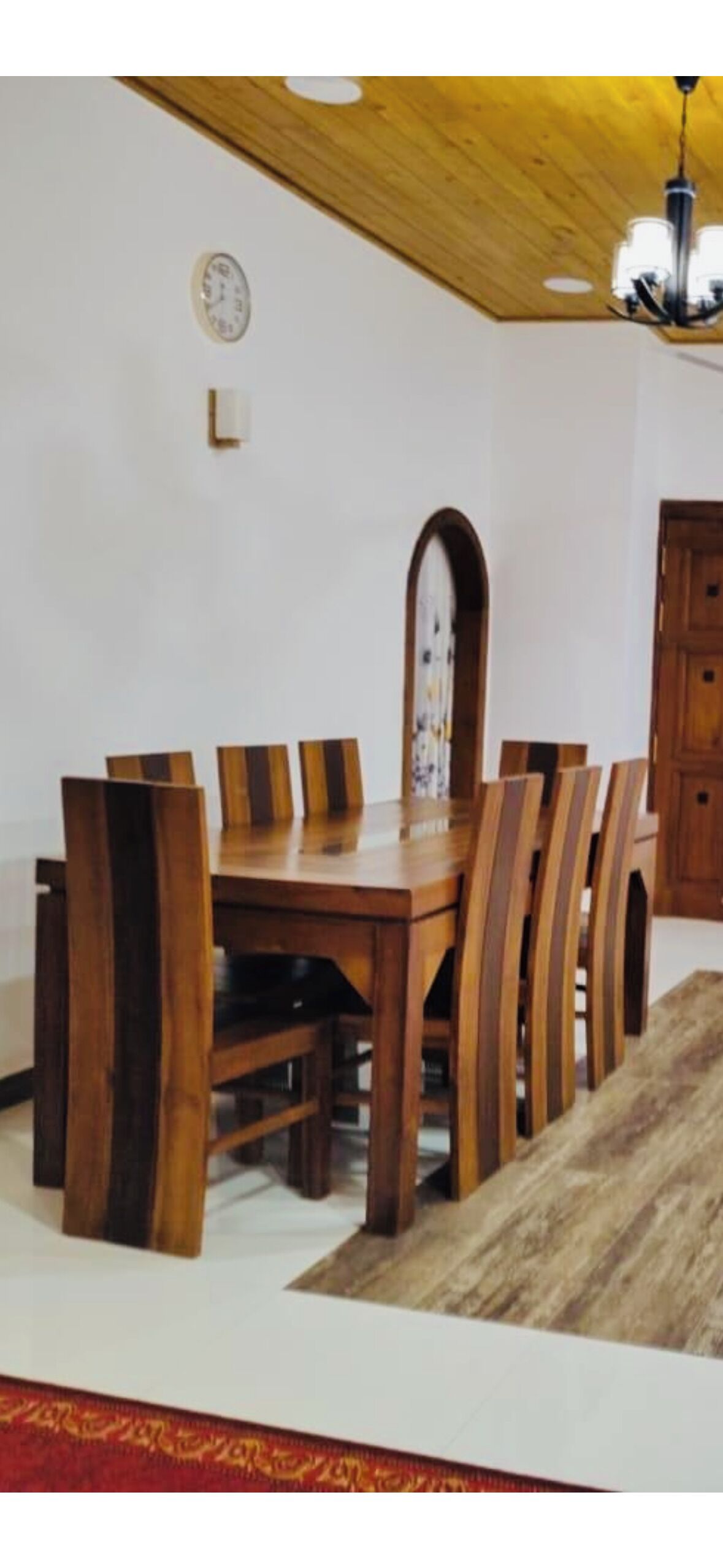 A dining area with a wooden table and chairs, a clock on the wall, and a chandelier.