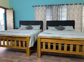 Deux lits en bois avec des têtes de lit, un banc en bois et une vue sur une porte et des rideaux.