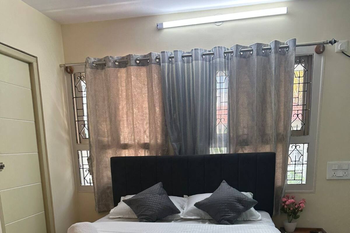 A bed with a headboard, a bedside table, a nightstand, and a window with curtains.