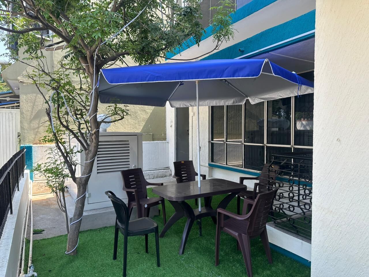 An outdoor patio with a table and chairs, a blue canopy, and a tree.