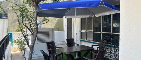 An outdoor patio with a table and chairs, a blue canopy, and a tree.