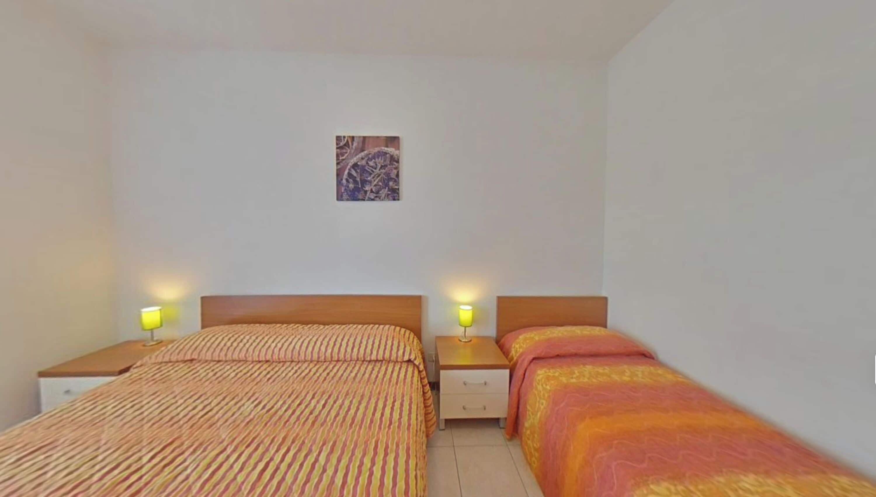 A simple room with two beds, a small table, and a wall-mounted picture.