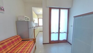 A compact living space with a sofa, a kitchenette, and a sliding glass door leading to a balcony. - Functional Flat in a Central Area (Lignano Sabbiadoro)
