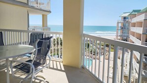 A balcony with a table and chairs, overlooking a beach and a pool area. - Cambridge 410 - Beautiful Condo in Litchfield by the Sea (Pawleys Island)