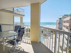 A balcony with a table and chairs, overlooking a beach and a pool area. - Cambridge 410 - Beautiful Condo in Litchfield by the Sea (Pawleys Island)