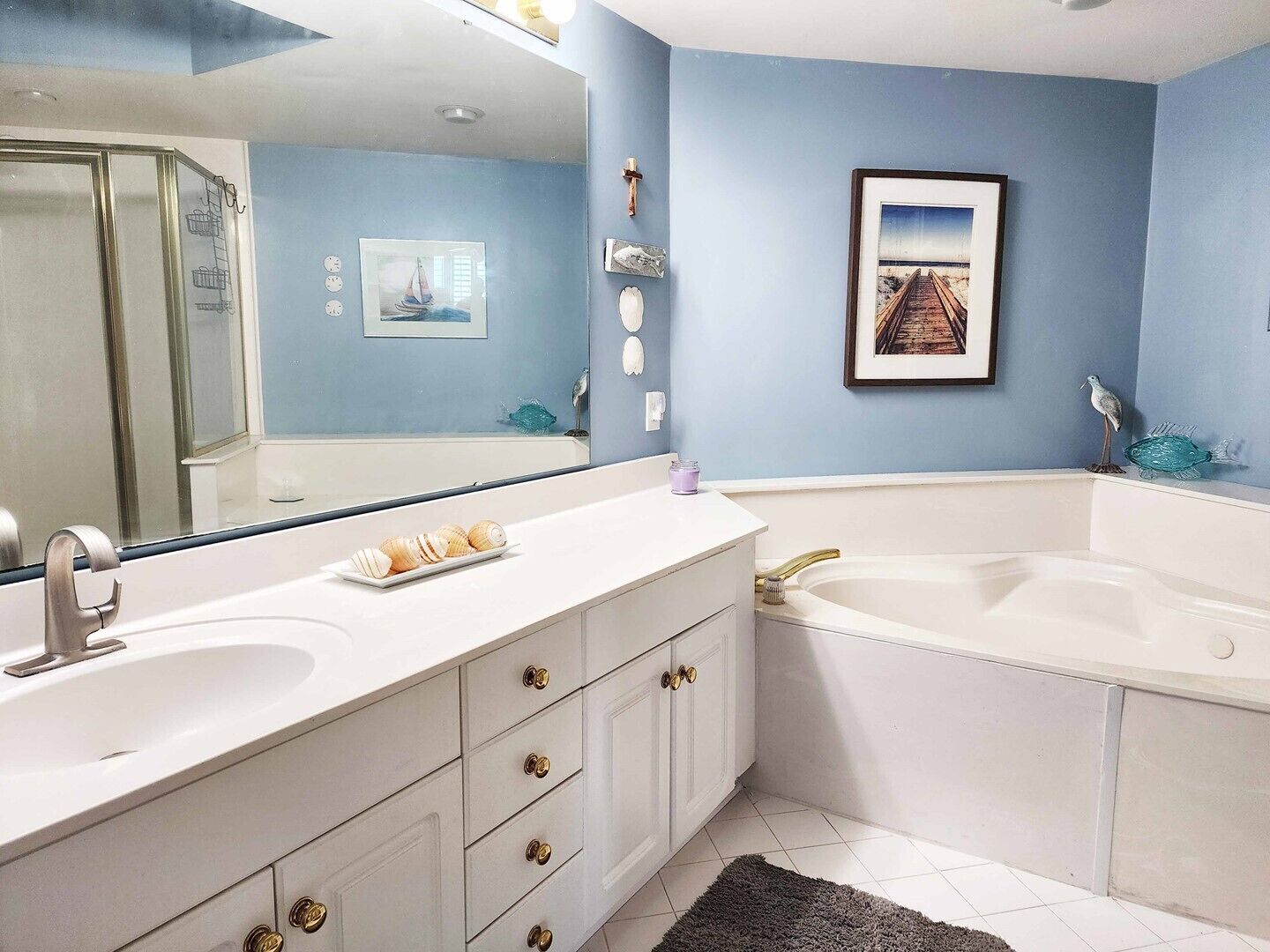 A bathroom with a large mirror, two sinks, a bathtub, and decorative items on the wall.
